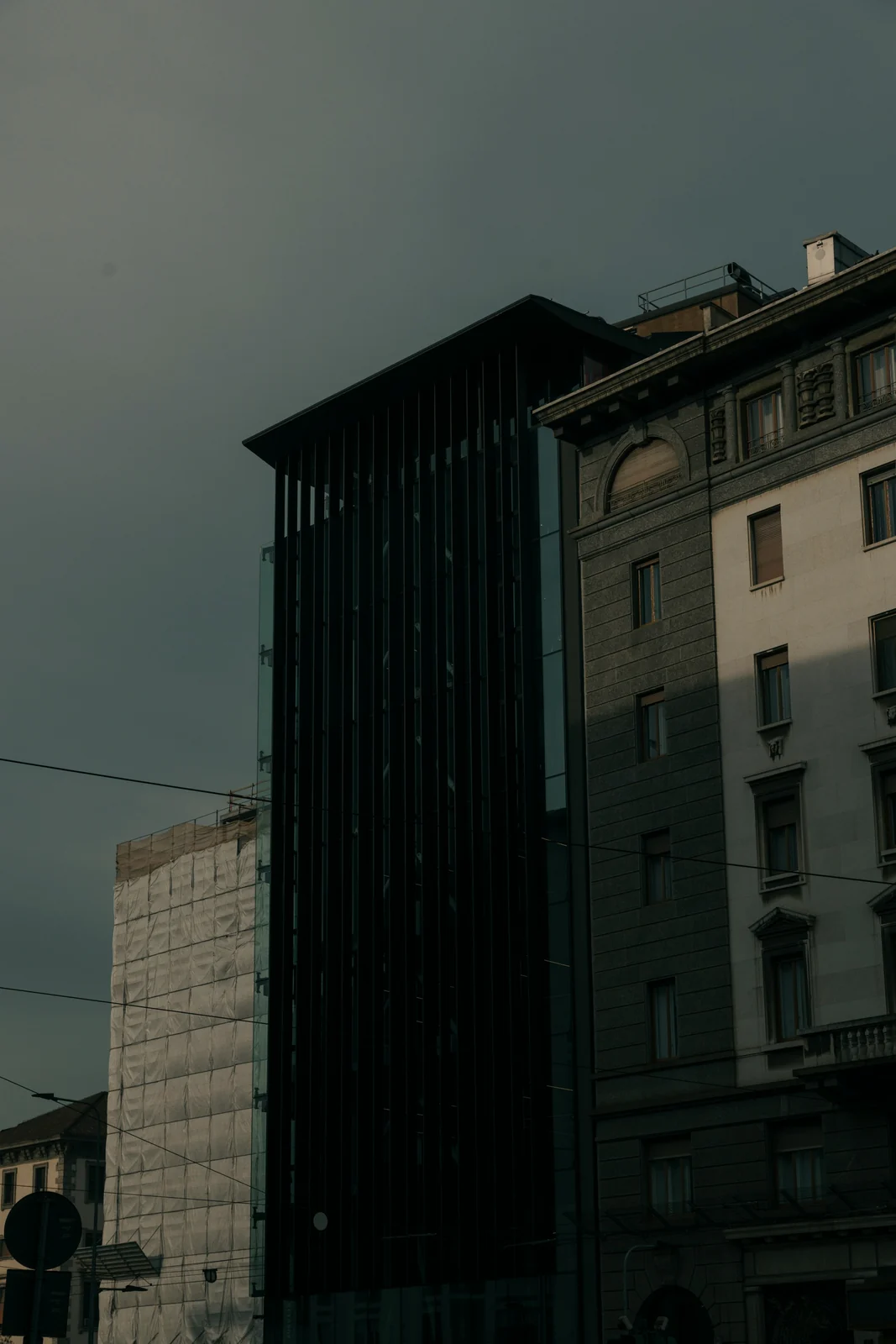 Modern dark tower beside historic and under-construction buildings